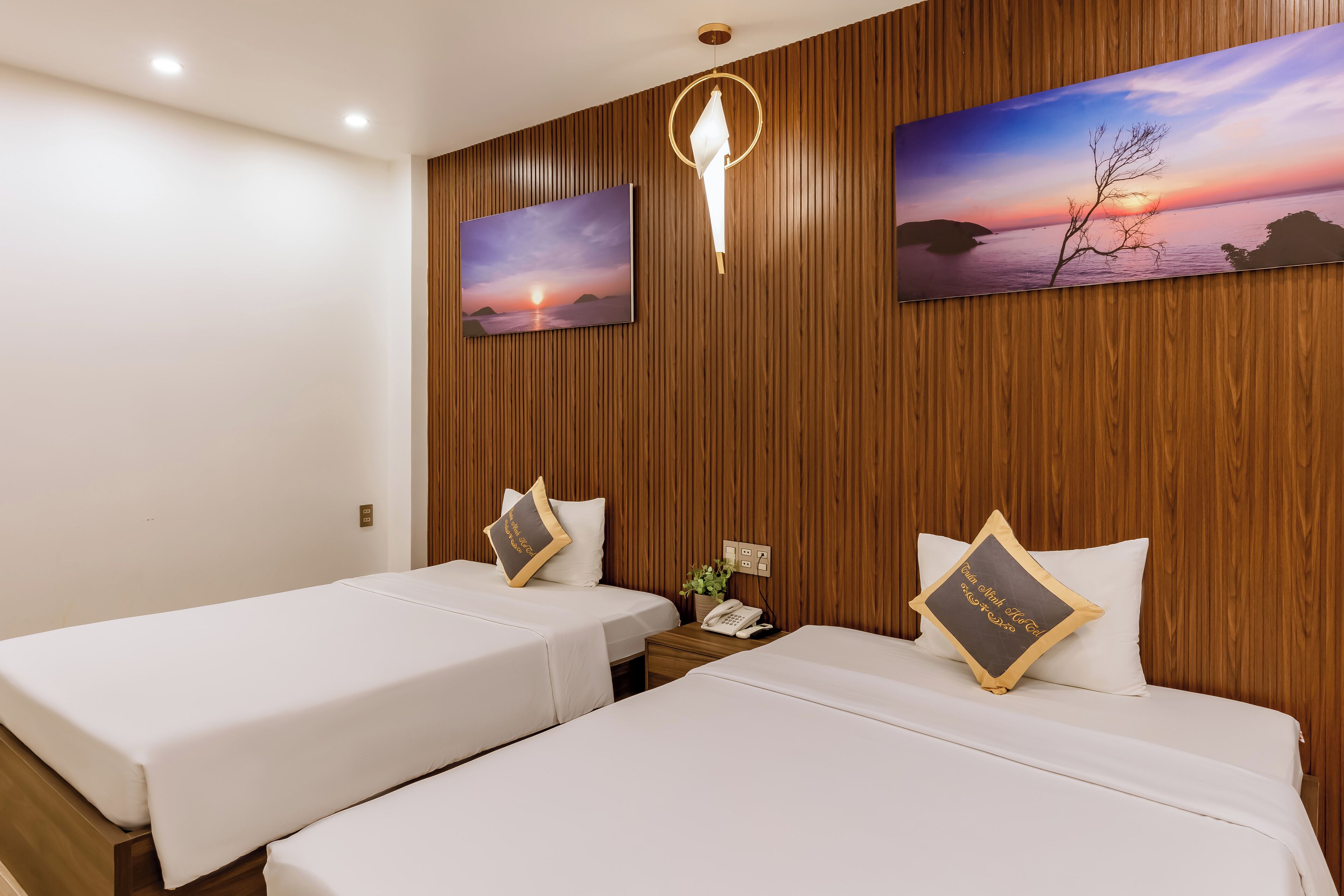 A hotel room with two beds, wooden paneling on the walls, and two paintings depicting sunsets.