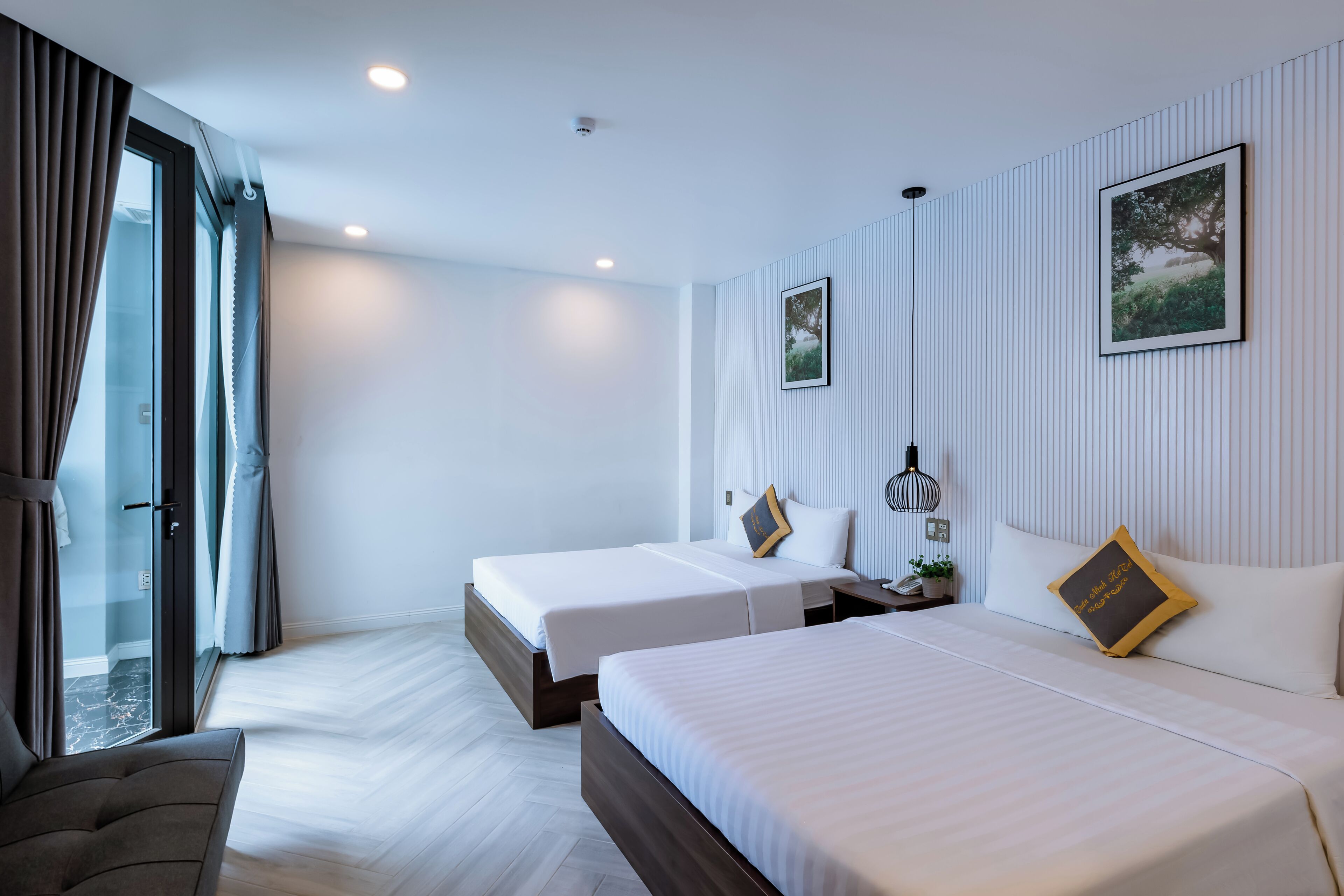 A hotel room with two beds, a large window with curtains, a sofa, and a wall-mounted picture.