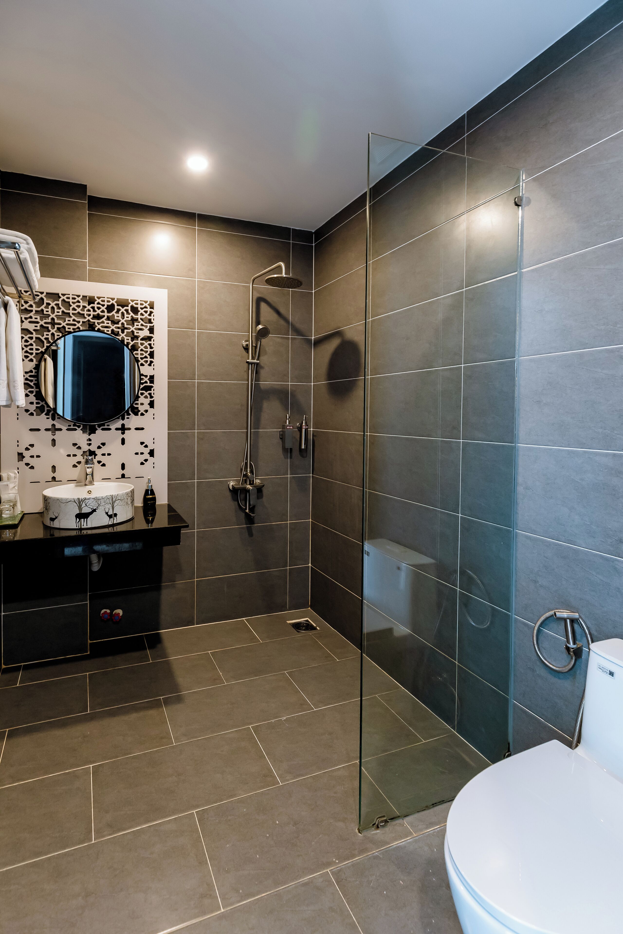 Une salle de bain moderne avec une douche à parois de verre, un miroir rond et un meuble-lavabo noir avec un vasque blanche.
