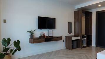 Una habitación moderna con un televisor montado, estanterías de madera empotradas, una planta en maceta y un suelo con estampado tipo espiga.