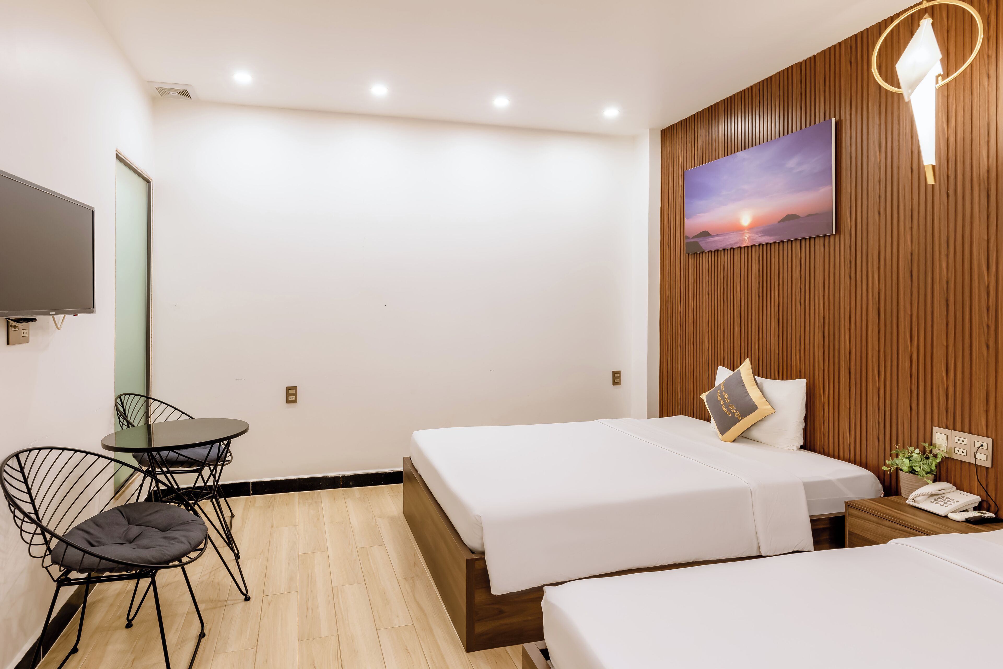 Habitación de hotel con dos camas, un escritorio con silla, televisión y una lámpara de pared.