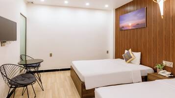 Habitación de hotel con dos camas, un escritorio con silla, televisión y una lámpara de pared.