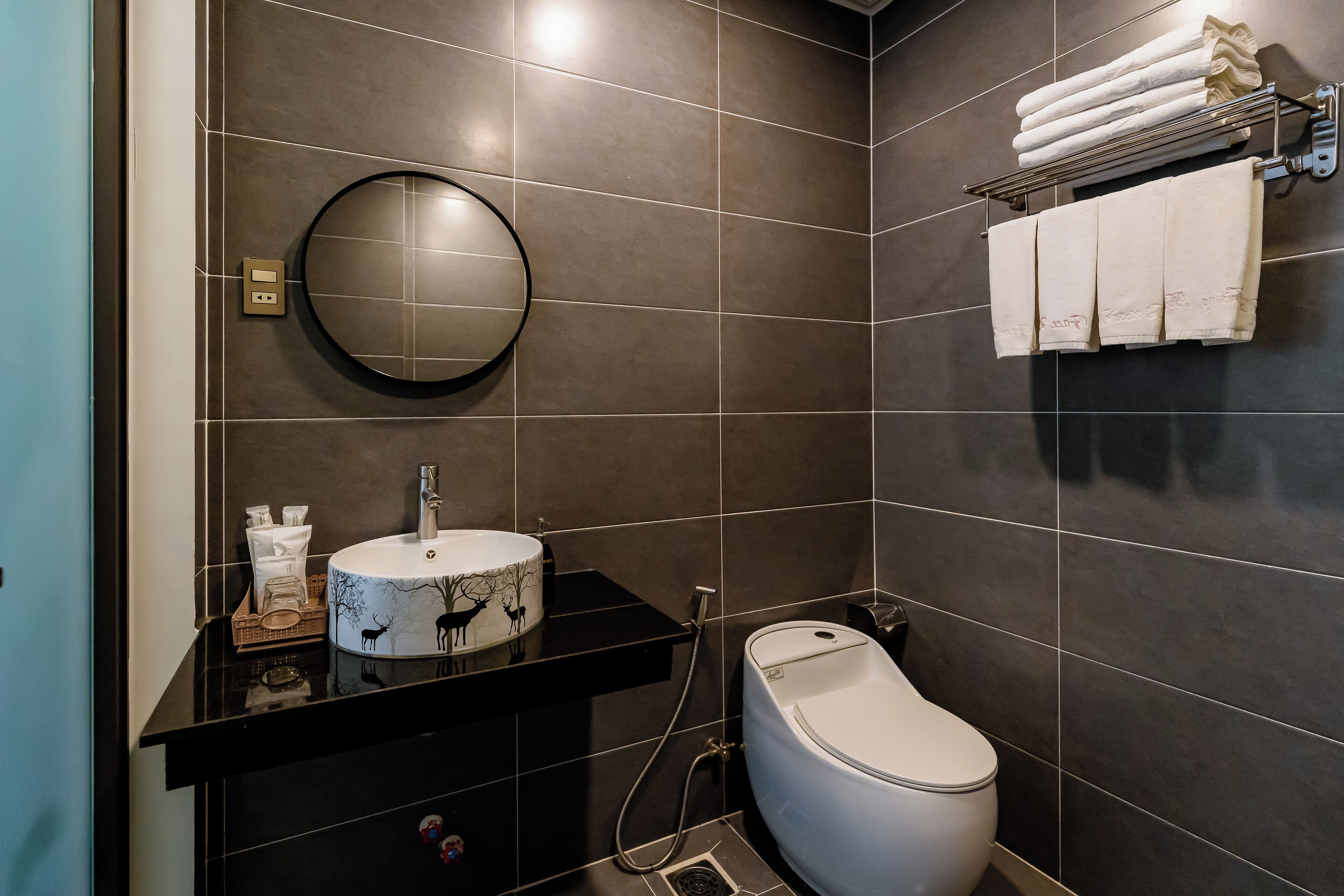 Une salle de bain moderne avec un miroir rond, des toilettes blanches et un porte-serviettes.