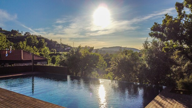 A swimming pool with a wooden deck, surrounded by trees and hills in the background.