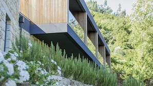 A modern building with a sloped roof and wooden paneling, surrounded by greenery and white flowers.