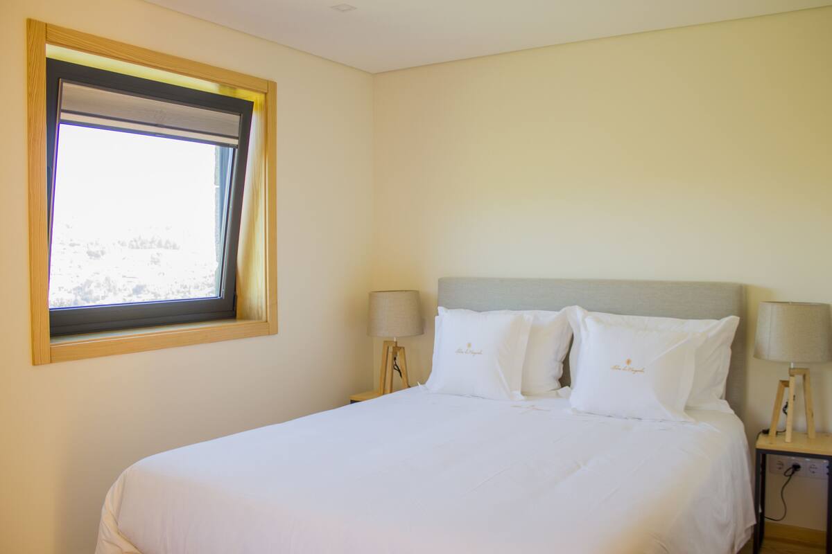 A neatly made bed with white linens and pillows, two bedside lamps, and a window with a view of a snowy landscape.