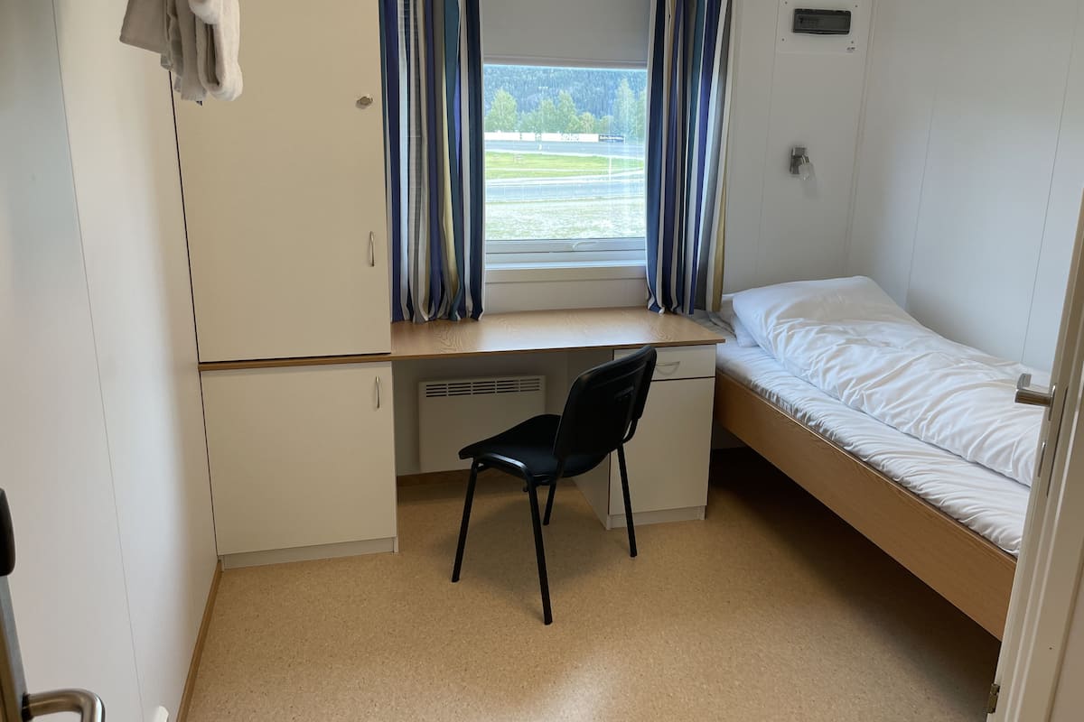 Una habitación pequeña con una cama individual, un escritorio con silla y un ventanal con cortinas.
