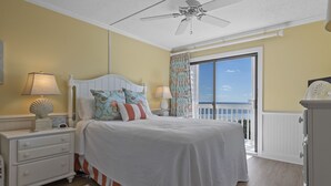 A bedroom with a bed, nightstands, a ceiling fan, a window with curtains, and a view of the outdoors.