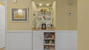 A room with a white built-in shelf unit containing various items, including a framed picture, glassware, and a thermostat.