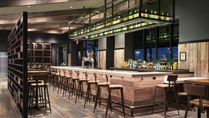 A bar area with wooden flooring, bar stools, and a high shelf displaying bottles. - Great Wolf Lodge Manteca (Manteca)