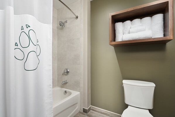 Un baño con cortina de ducha con estampado de huellas, una bañera, un estante de madera con toallas y un inodoro.