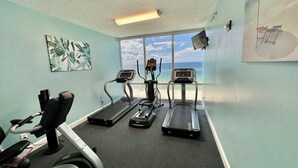 Un gimnasio con cintas de correr, una bicicleta estática y una máquina de remo, con vistas a la playa a través de amplias ventanas.
