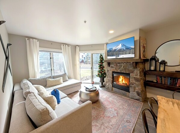 Una sala de estar acogedora con chimenea de piedra, un televisor de pantalla plana grande, un sofá cómodo y un árbol de Navidad.