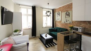 Un soggiorno moderno con un divano verde, un tavolino da caffè, una TV e un angolo cottura con un forno a microonde.