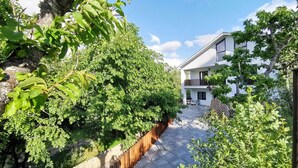 Ein modernes Haus mit gepflasterter Terrasse, umgeben von üppiger Vegetation und einem Holzzaun.