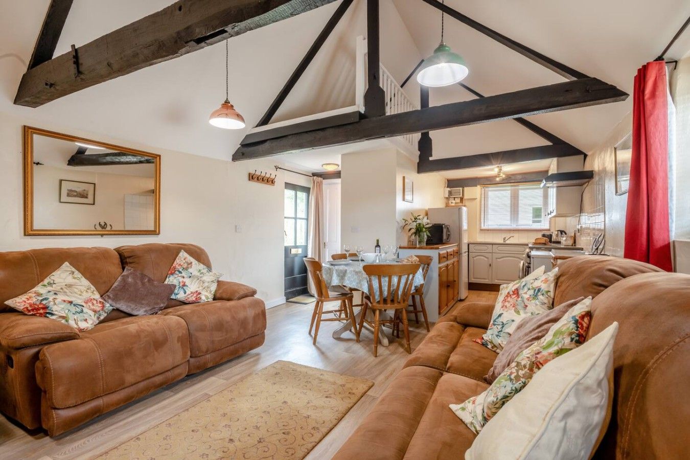 A cozy living room with brown leather sofas, a dining table, and a kitchen area with a microwave and sink.