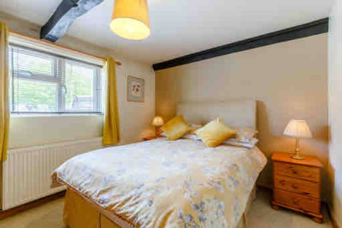 Une chambre à coucher avec un lit, des lampes de chevet, une commode et une fenêtre avec des rideaux.