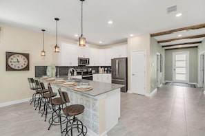 A modern kitchen with a central island, bar stools, and pendant lighting. - Game, Themed Rooms, Theater 8BR Pool Home near WDW (Kissimmee)