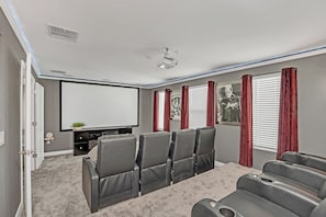 A home theater room with a large screen, multiple seating, and a ceiling projector. - Game, Themed Rooms, Theater 8BR Pool Home near WDW (Kissimmee)