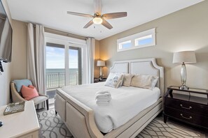 A hotel room with a large bed, a ceiling fan, a view of the ocean, and a balcony.