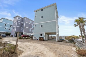 A beachfront property with multiple-story buildings, a sandy driveway, and a wooden fence.