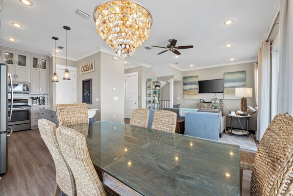 A modern kitchen with stainless steel appliances, a dining area with a glass table and wicker chairs, and a ceiling fan. - Gulf Front Home with Pool! (Cape San Blas)