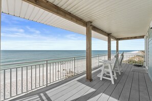 A covered wooden deck with white railings overlooking a beach. - Gulf Front Home with Pool! (Cape San Blas)