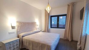 A bedroom with a bed, nightstands, a chandelier, and a window with curtains.