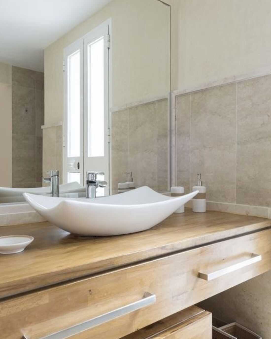 Un baño moderno con un lavabo de pedestal grande, tocador de madera y un espejo amplio.