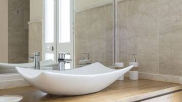 Un baño moderno con un lavabo de pedestal grande, tocador de madera y un espejo amplio.