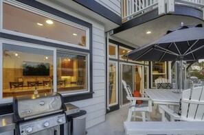 Eine Terrasse im Freien mit Grill, weißer Möbel und einem großen Sonnenschirm.