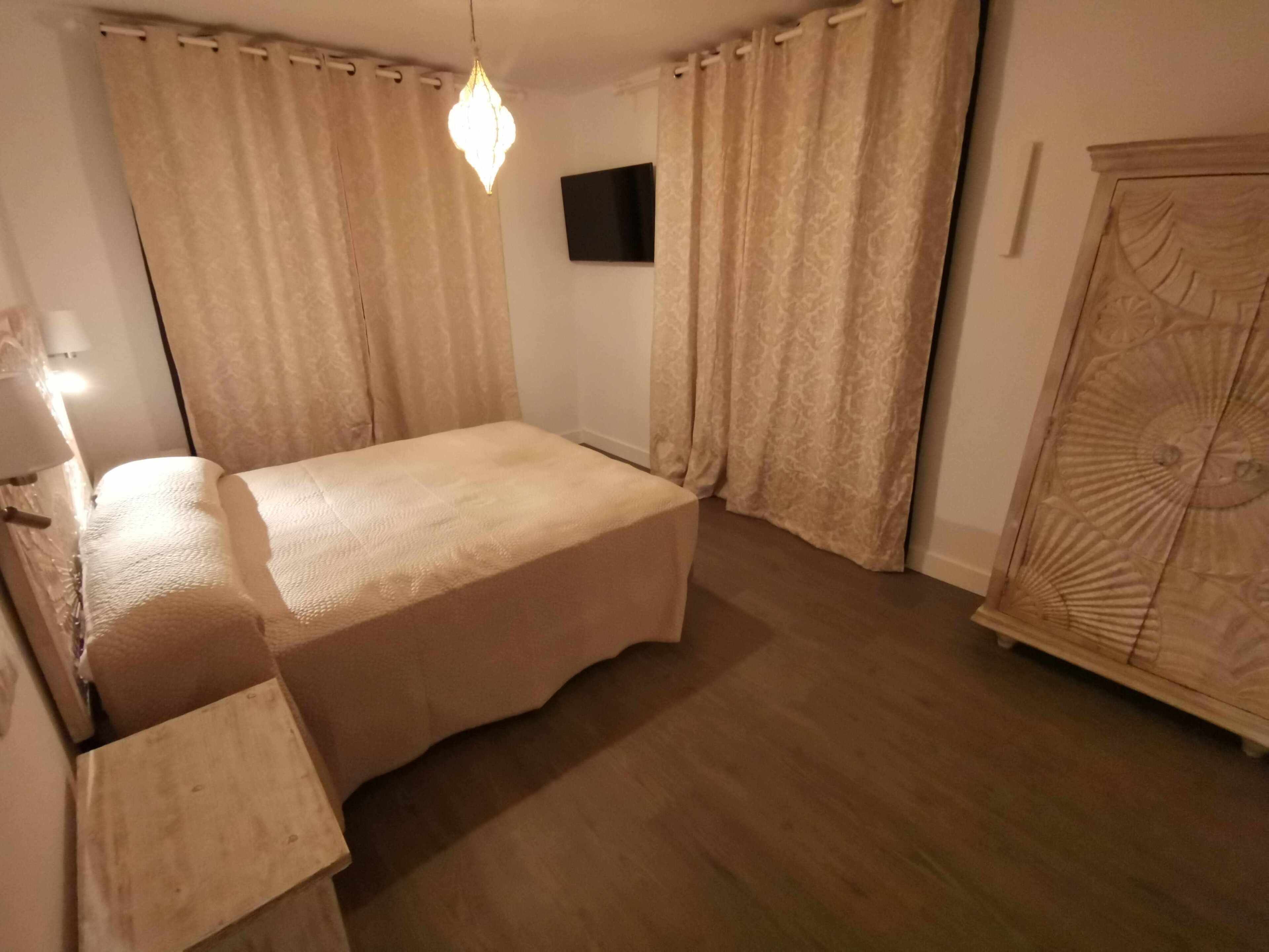 Una camera da letto con un letto, tende, un armadio in legno e una TV a parete.