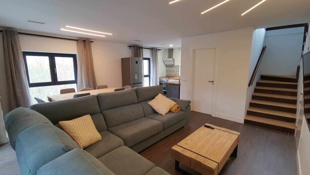 A modern living room with a sectional sofa, a wooden coffee table, and a dining area in the background.
