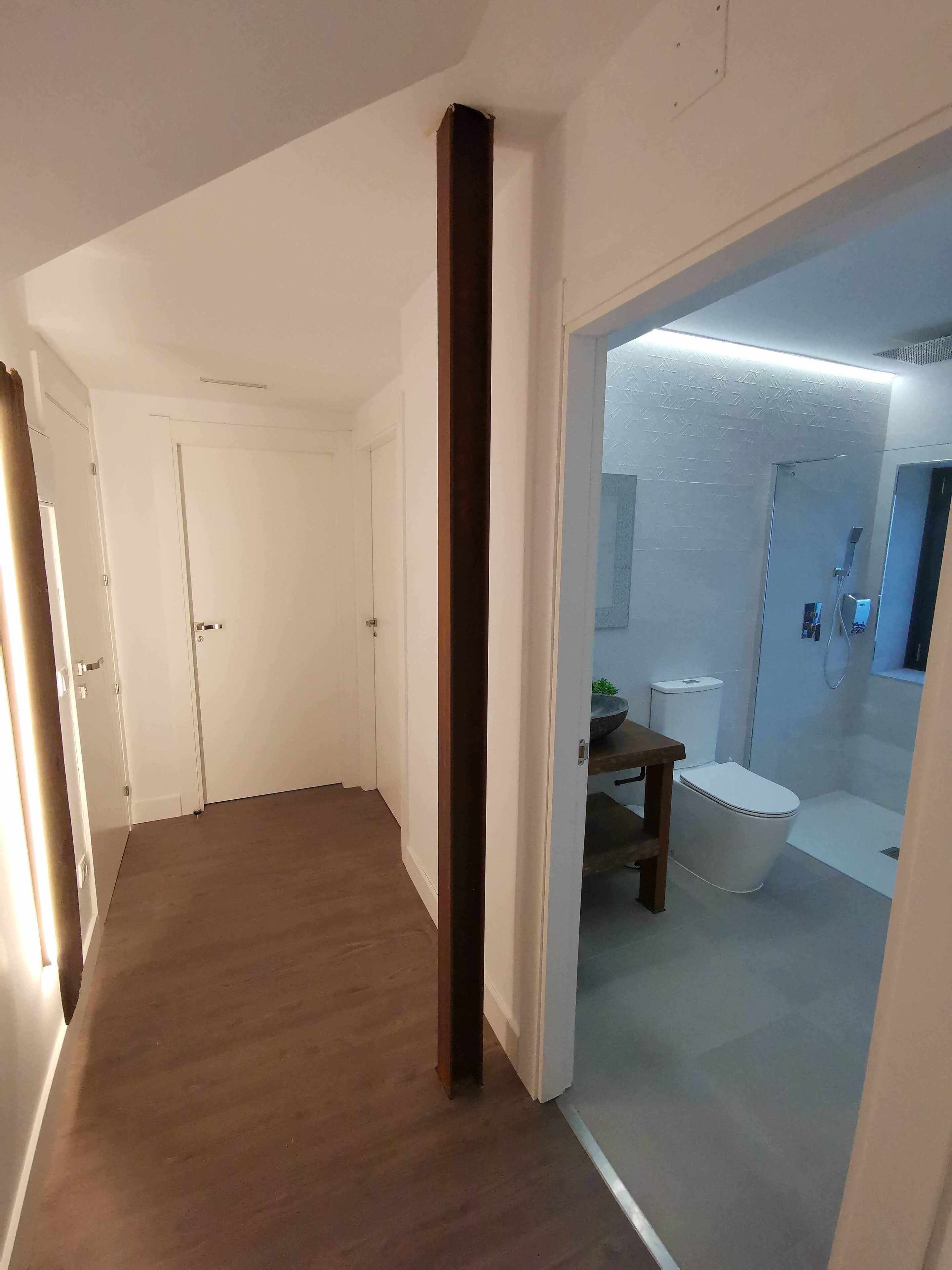 Un couloir menant à une salle de bain équipée d’une baignoire, de toilettes et d’un lavabo.