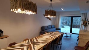 A modern dining area with a long wooden table, chairs, and a hanging light fixture.