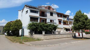 Un edificio residencial de varios pisos con balcones, un muro de piedra y un cielo azul despejado.