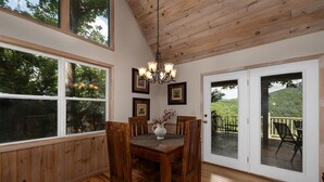 Un comedor con una mesa y sillas de madera, una araña y vistas al exterior a través de amplias ventanas y un ventanal corredizo.