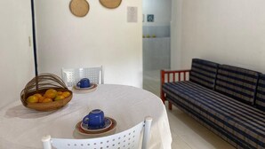 A dining area with a round table, chairs, a basket of fruit, and a sofa in the background.