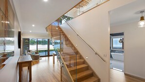 A modern interior with a wooden staircase, a glass railing, and a view of the outdoors.
