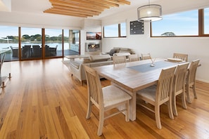 Un salón amplio con mesa de comedor de madera, asientos cómodos, chimenea y ventanas grandes que ofrecen vistas al exterior.