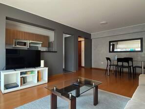 A modern living room with a flat-screen TV, a glass coffee table, and a dining area with chairs. - w* | Charming 2BR in Miraflores (Lima)