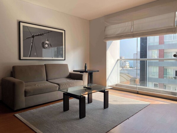 A modern living room with a sofa, a glass coffee table, and a framed picture on the wall. - w* | Charming 2BR in Miraflores (Lima)