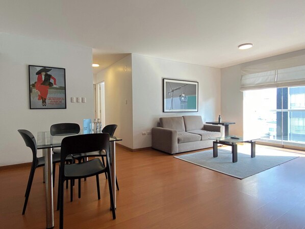 A modern living room with a dining area, a sofa, and a coffee table. There are two framed pictures on the walls. - w* | Sleek 2BR in Iconic Miraflores (Lima)