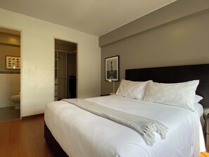A neatly made bed with white linens and a patterned throw blanket, a dark headboard, and a framed picture on the wall. - w* | Charming 2BR in Miraflores (Lima)