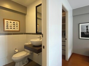 A modern bathroom with a white sink, toilet, and a framed picture of hats on the wall. - w* | Charming 2BR in Miraflores (Lima)