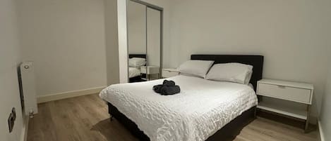 A bedroom with a large bed, a nightstand, a mirror, and a wardrobe.
