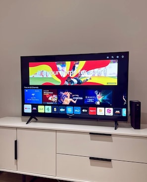 A flat-screen TV on a white cabinet with a digital interface displaying various channels and a sports event. - Solihull Studio • WiFi • NEC • BHX (Solihull)