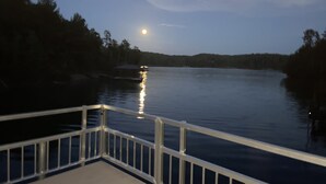 A wooden deck with a railing overlooking a calm body of water at dusk.