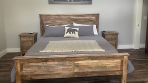 A wooden bed with a gray bedspread, two pillows, and a throw blanket.