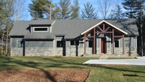 A modern two-story house with a stone facade, a large front porch with wooden beams, and a garage.
